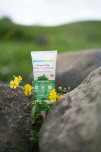 Oil-free face moisturizer from Mama Earth placed outdoors among rocks and yellow flowers.