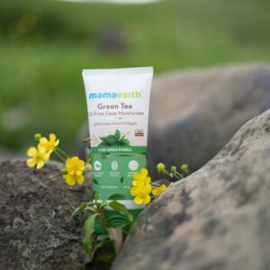 Oil-free face moisturizer from Mama Earth placed outdoors among rocks and yellow flowers.